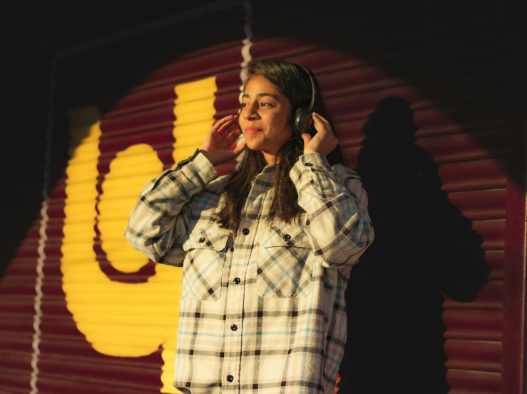 a girl wearing headphones is standing in front of a yellow and red sign