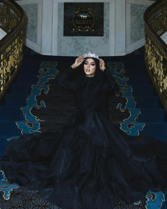 a woman dressed in a long black dress sits on blue stairs