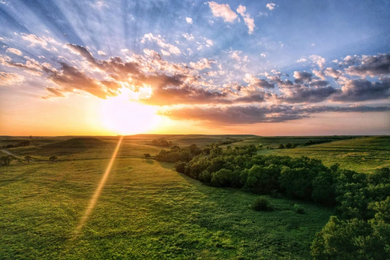 a sunset with sun in the clouds, and lush green fields