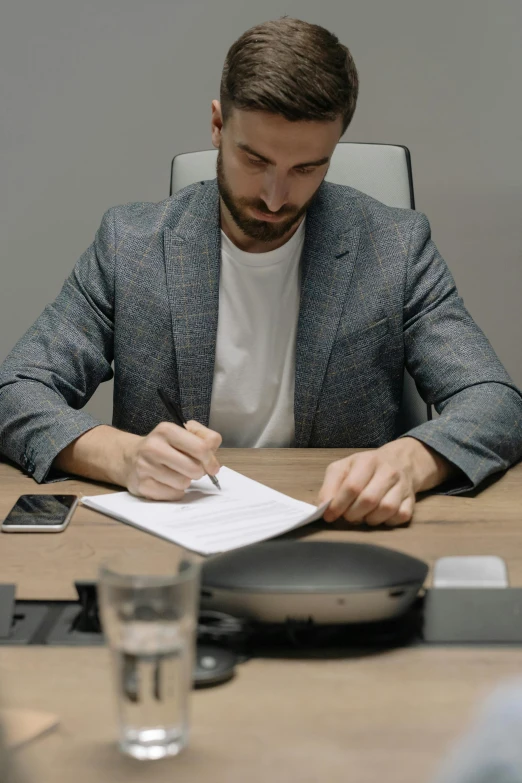 a man writing on a piece of paper sitting at a table with an open cell phone in the background