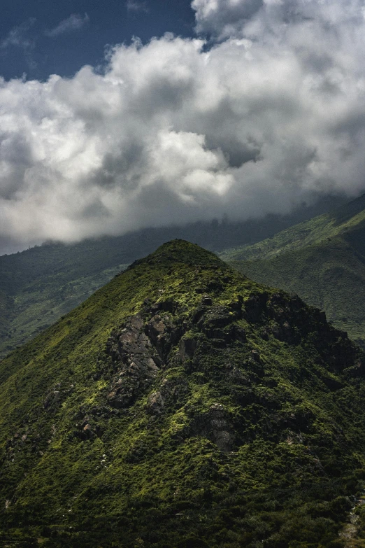 a very pretty green mountain with some clouds in the sky