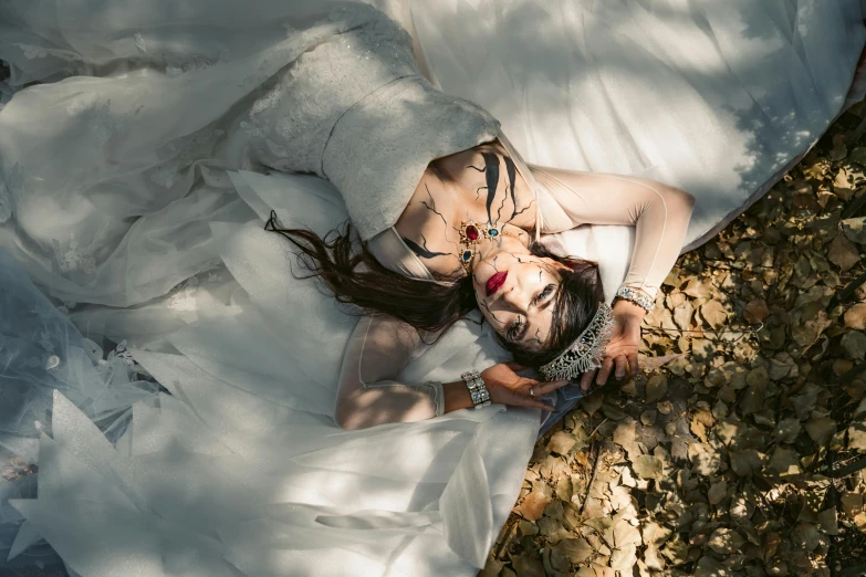 a woman in white lingerie laying on the ground covered with leaves