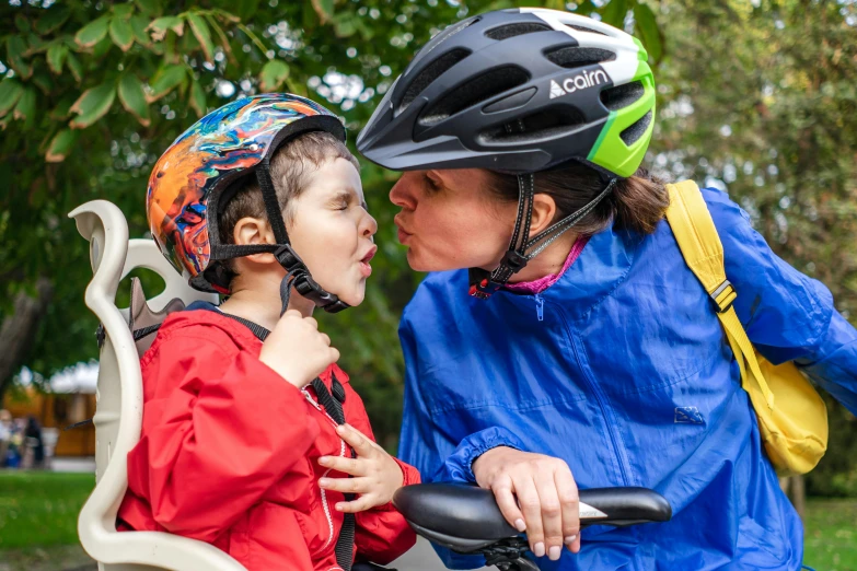 a woman kissing a young child with helmets on