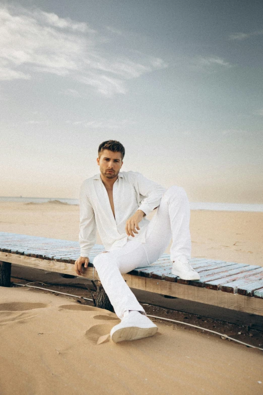 a man posing in front of a wooden dock on the beach