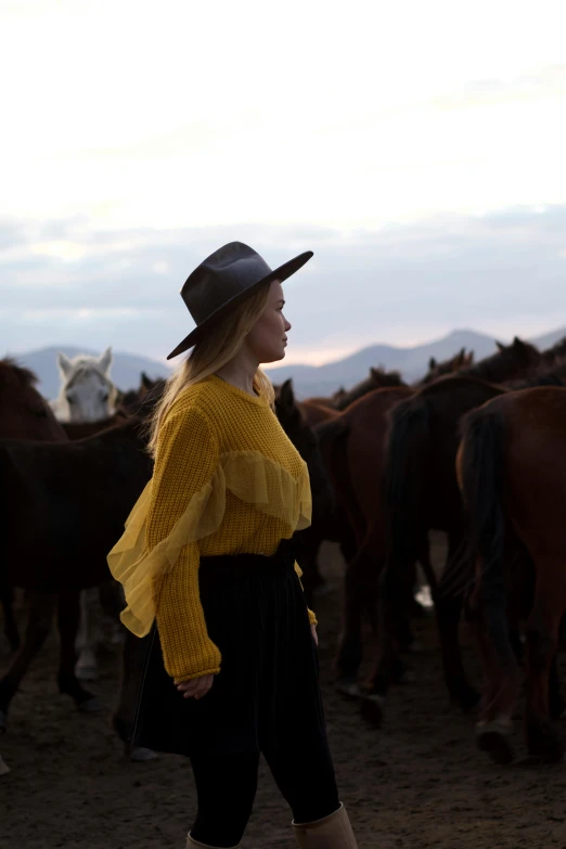 a woman walks through a field with a group of horses