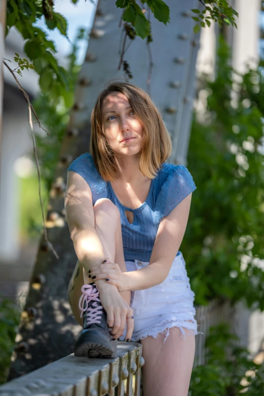 a woman sitting on the edge of a railing wearing a blue shirt and white shorts