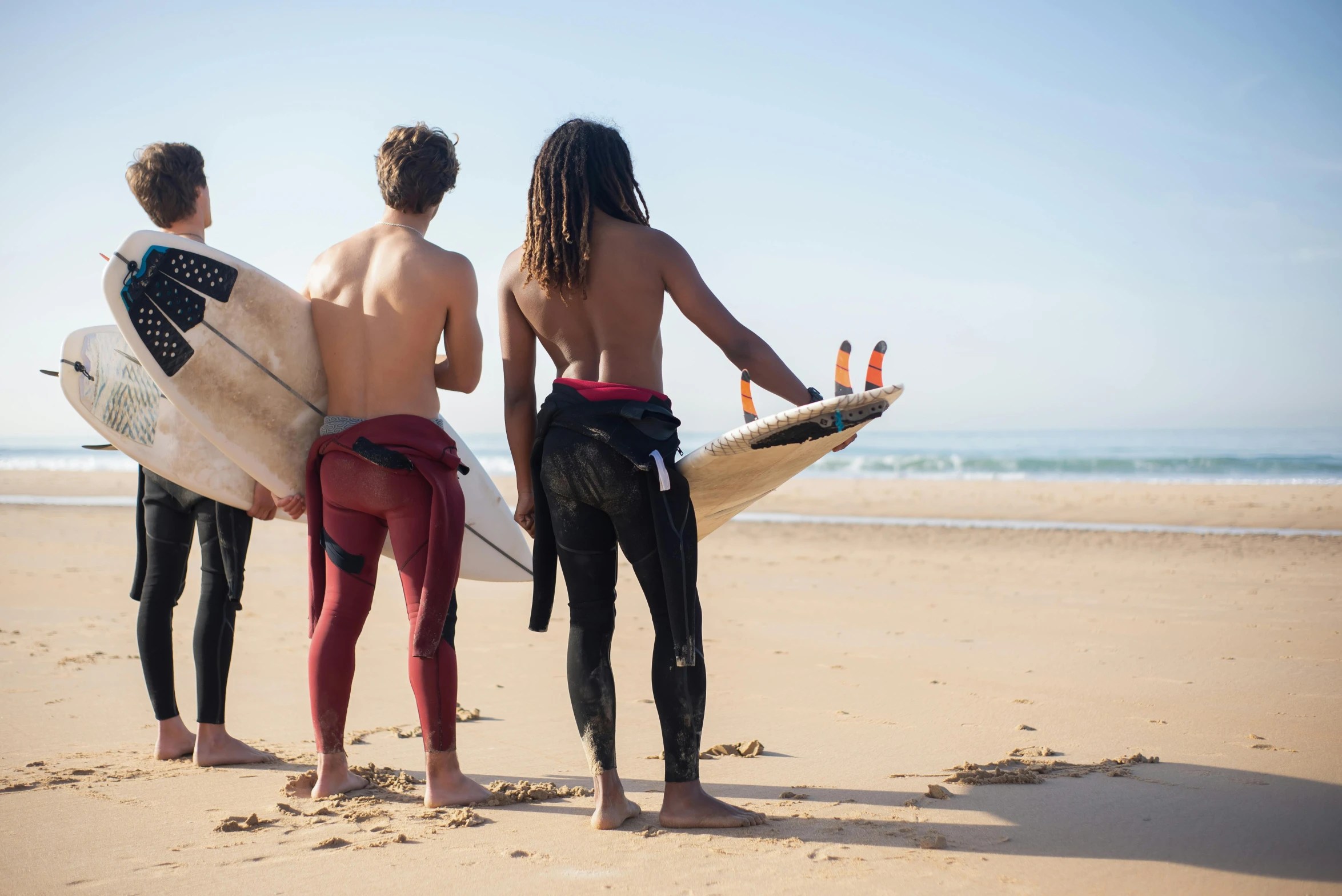 three people are standing on the beach holding surfboards