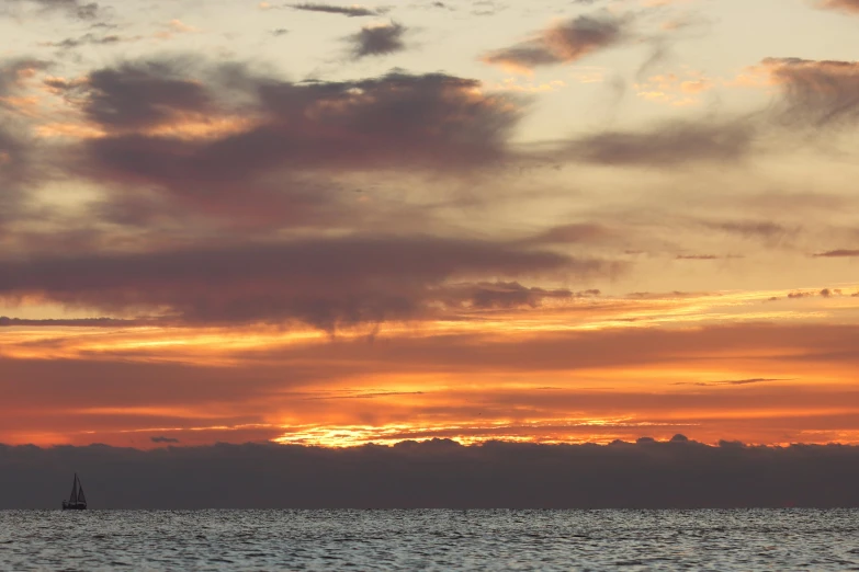 a boat floating in the water under a cloudy sunset