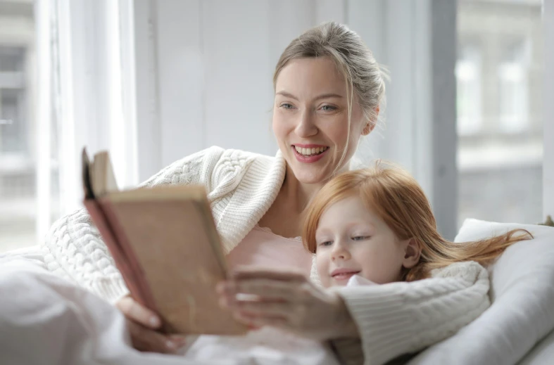 a woman and a child are laying on the bed reading a book