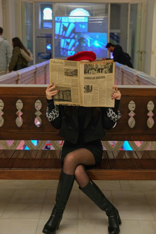 a woman sitting on a bench holding up a large newspaper