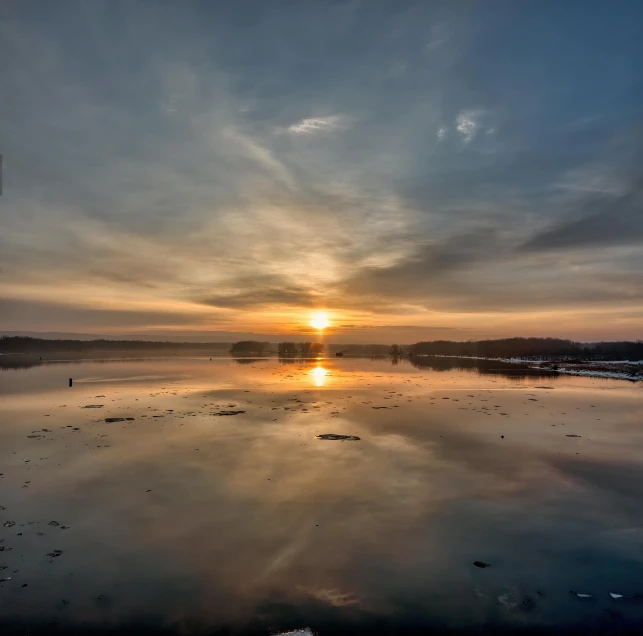 a lake with ice on the shore and sun setting