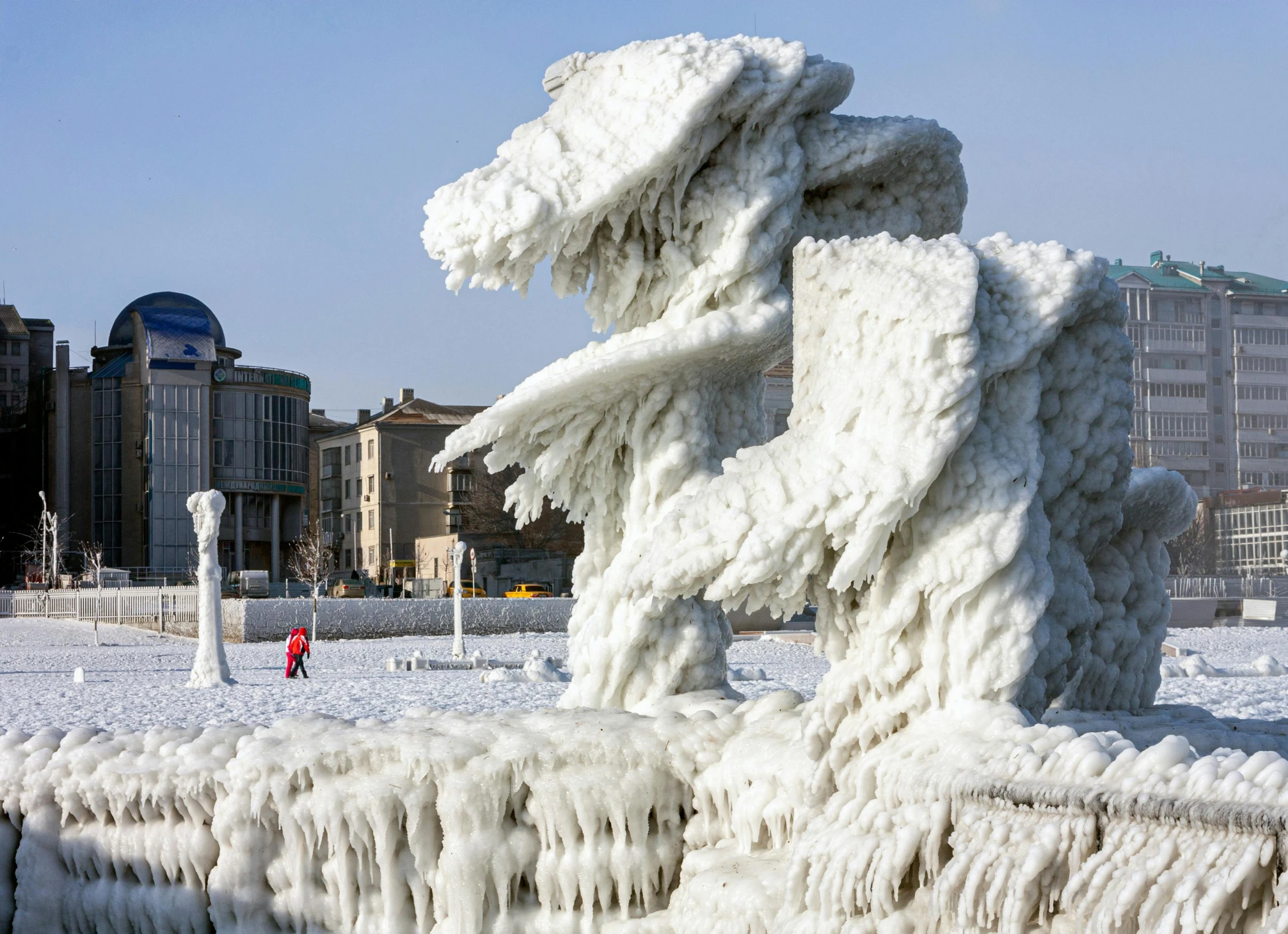 an ice sculpture on a snowy field with buildings in the background