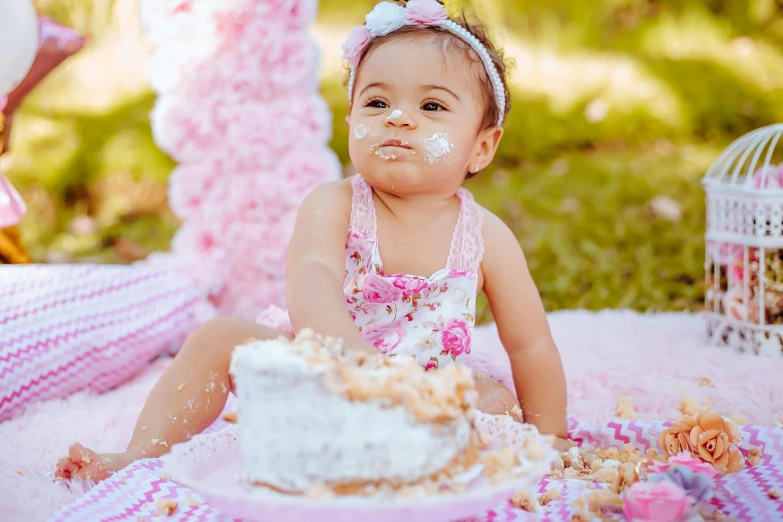 a baby sits on a blanket with cake on her face