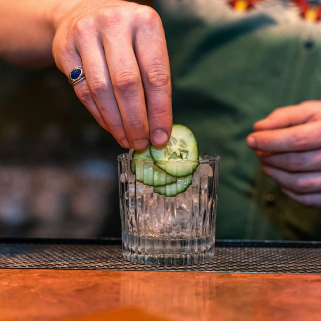 someone putting cucumber in a glass to drink