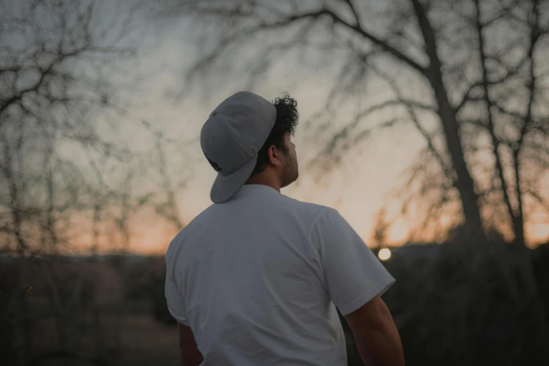 a man standing next to a tree watching the sunset