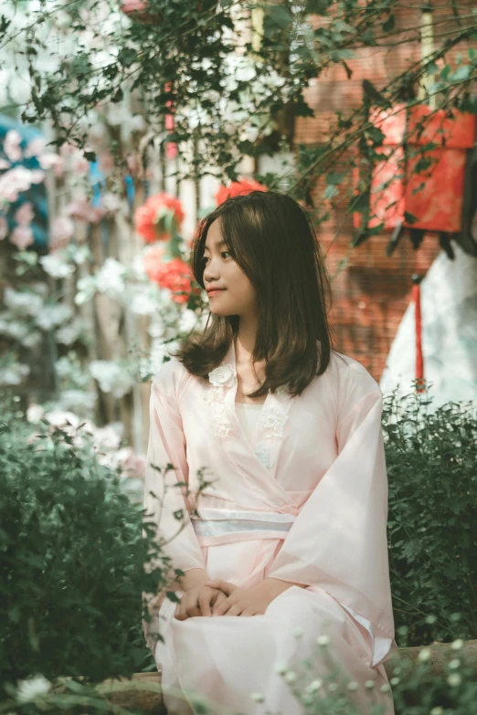 a woman sitting on a bench outside, wearing a pink dress