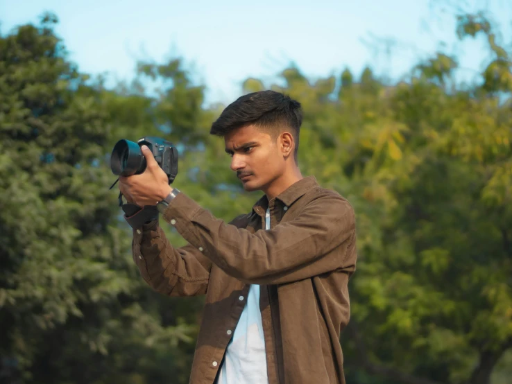 a man holding up a camera with trees in the background