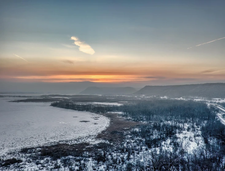 a sunset over some snowy woods and water