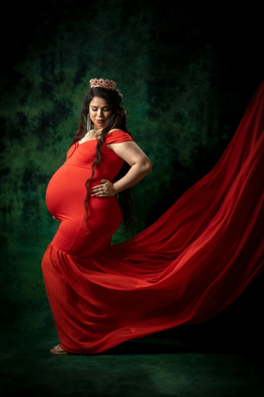 a pregnant girl wearing red poses for a studio portrait