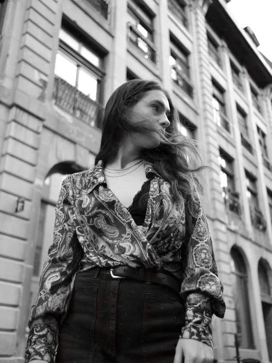 black and white pograph of a woman in a paisley shirt outside a building