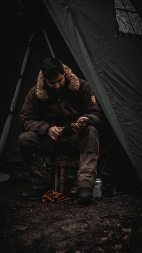 a man sits in front of his tent with his phone
