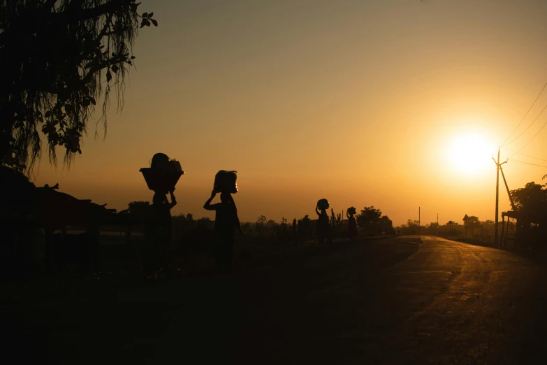 silhouetted people and their belongings walking down the street during a sunset