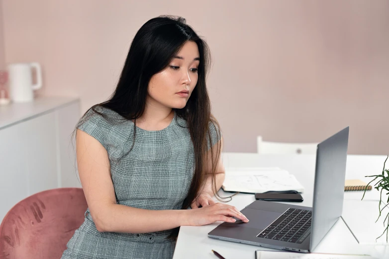 the woman in a grey dress is working on her laptop