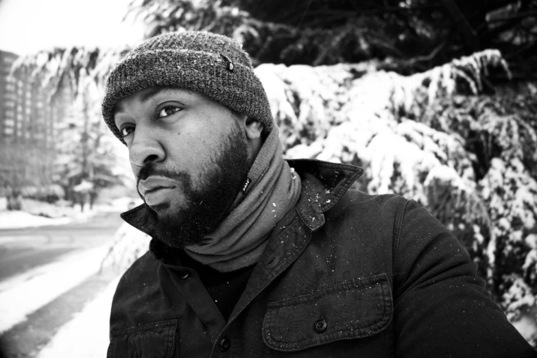 black and white pograph of a man standing in front of a snow covered tree