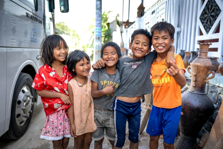 four young children hugging on the sidewalk near a large yellow bus