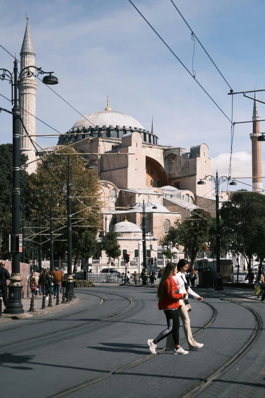 two people walking on the road in front of an elaborate building