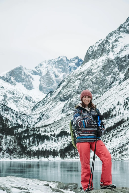 a girl in a ski jacket standing on a mountain near water