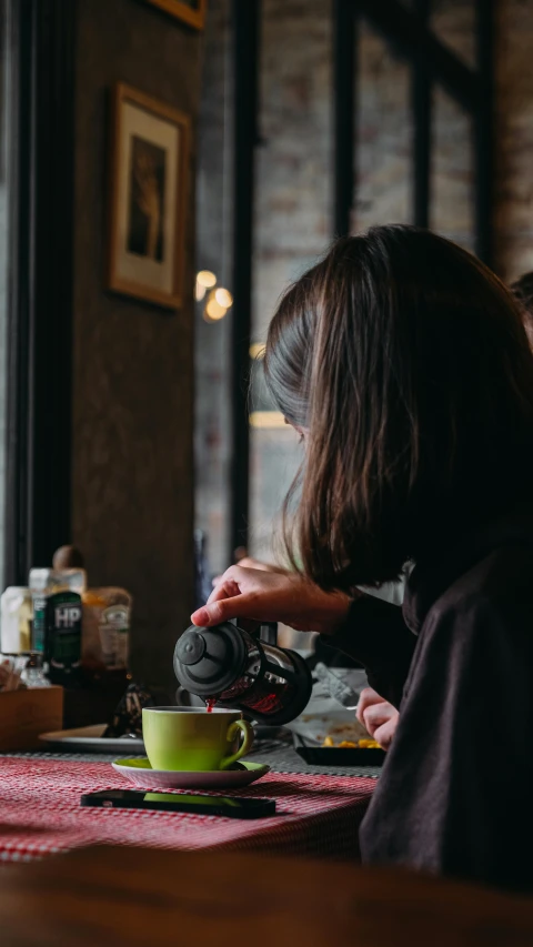 woman pouring coffee into a green cup on a red and white table cloth