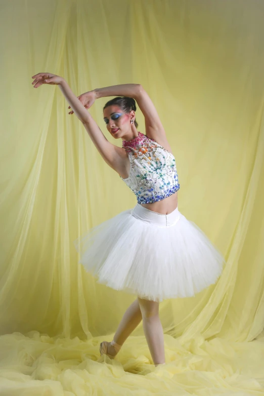 young ballerina dancer wearing tulle and crop top, dancing, against yellow background