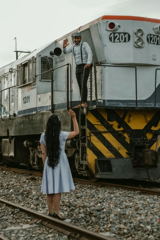 woman is standing next to train on the tracks and another person is leaning forward