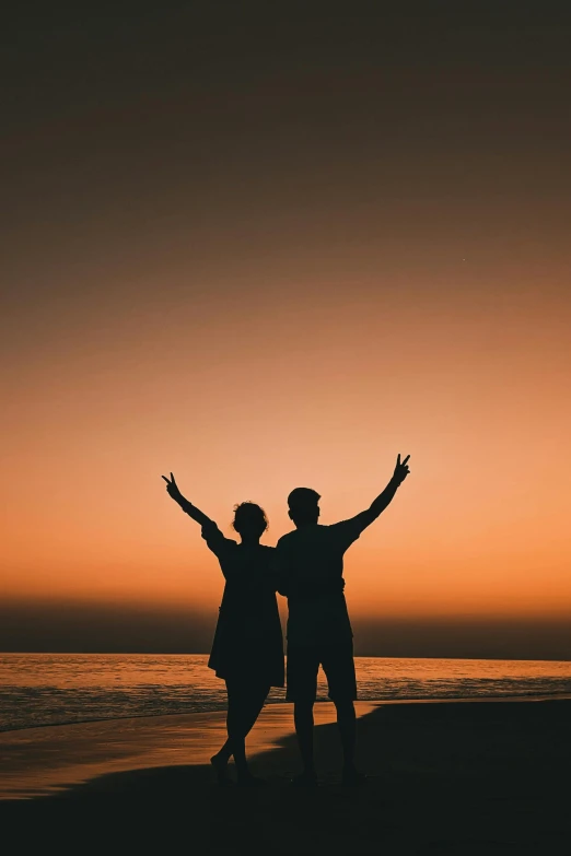 couple on beach arms up at sunset silhouette