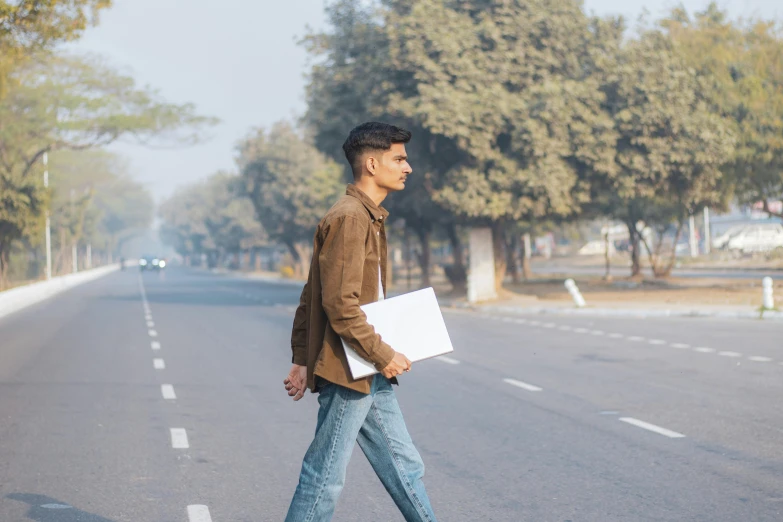 a man is walking on the road with his laptop