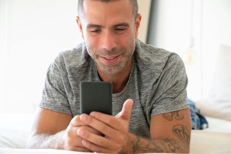 the man looks at his cell phone while laying on a bed