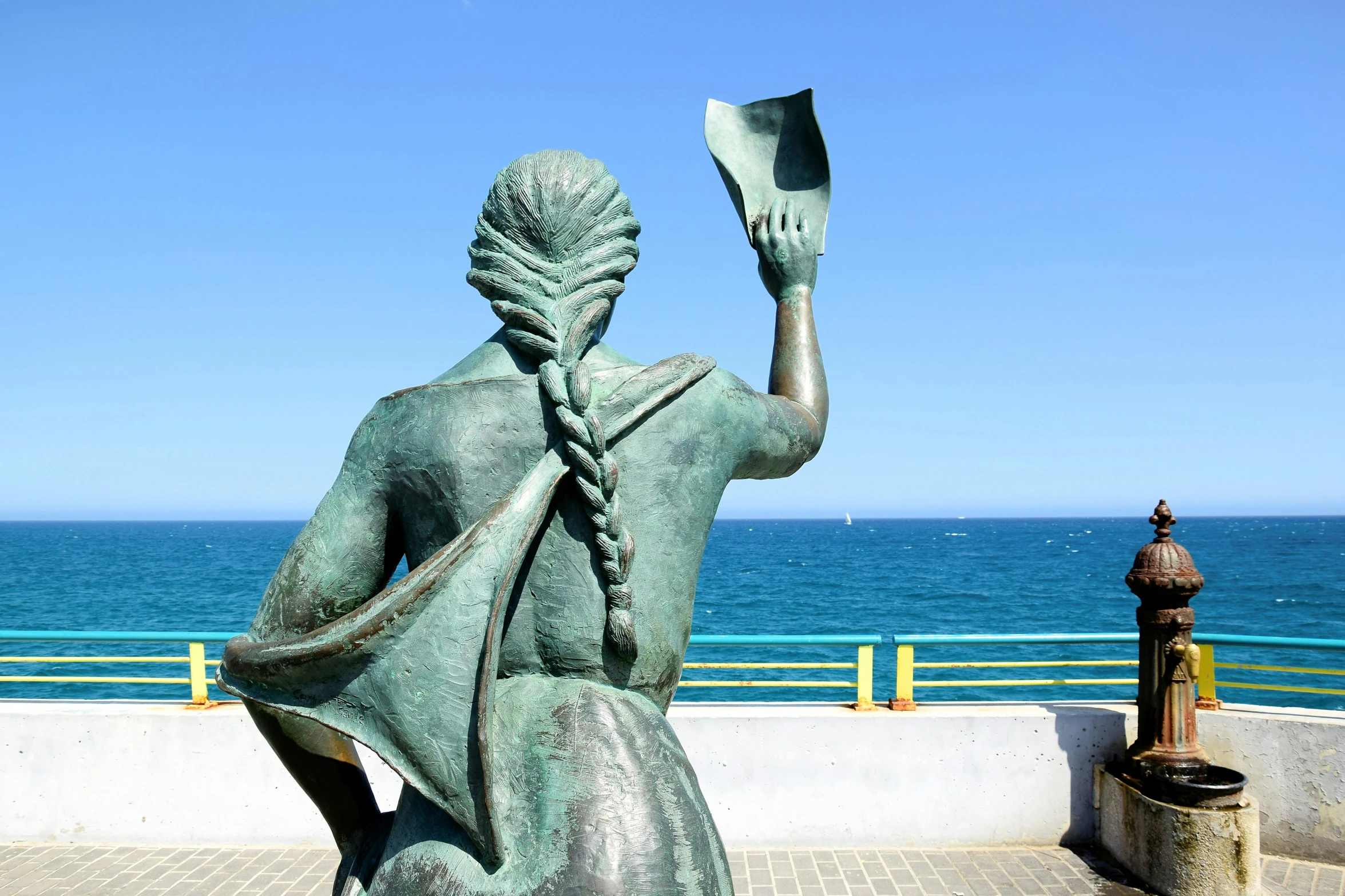 a statue sitting by the water holding a book