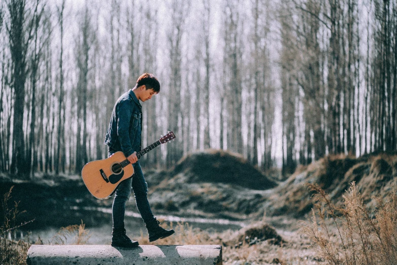 a man with an acoustic guitar standing on a rock