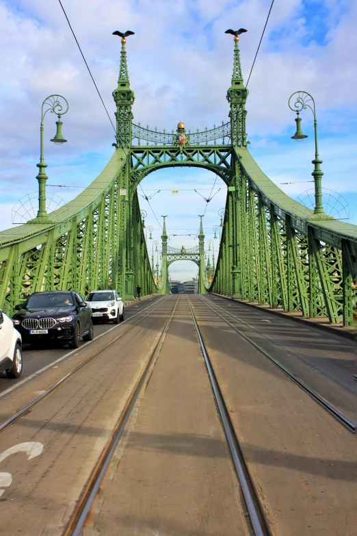 cars are traveling across a green bridge during the day