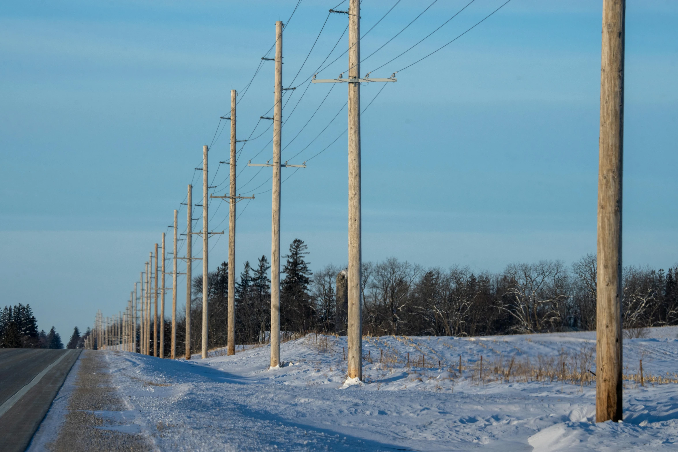 multiple power poles and telephone wires on the side of a snow covered road