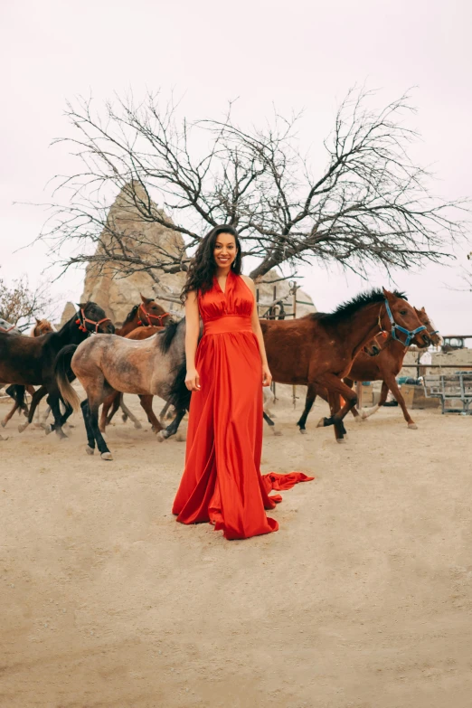 a woman in a red dress standing next to a group of horses