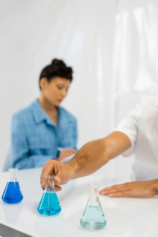 two people wearing blue shirts stand in front of two test tubes that are filled with water