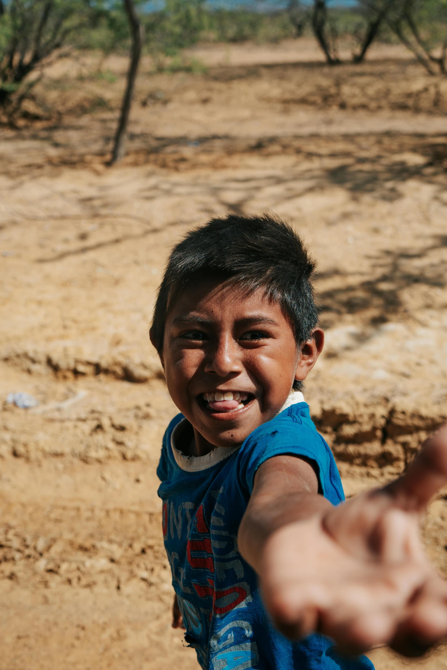 a boy pointing his hand at someone on a dirt field