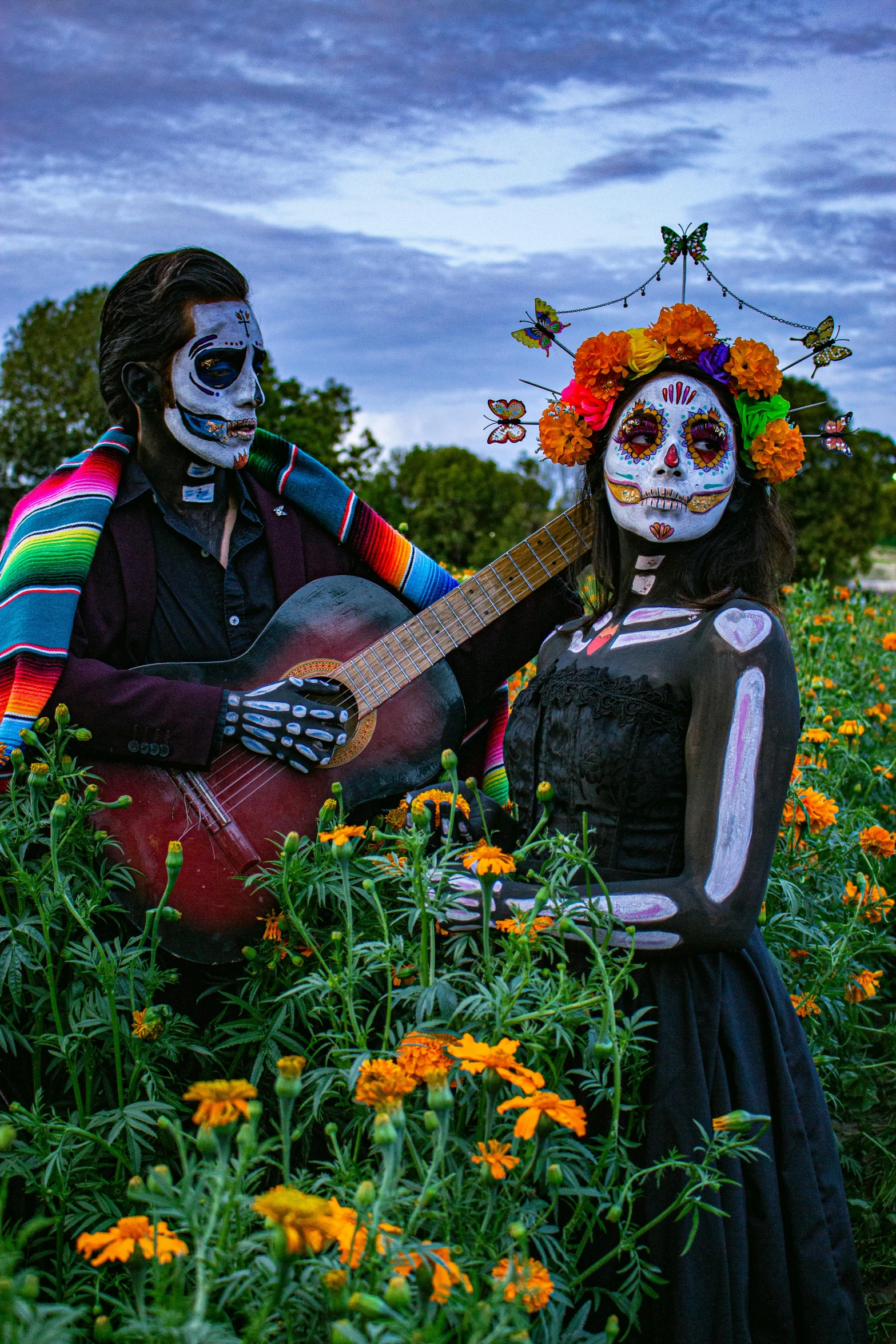 couple in skeletons costumes holding an acoustic guitar outdoors