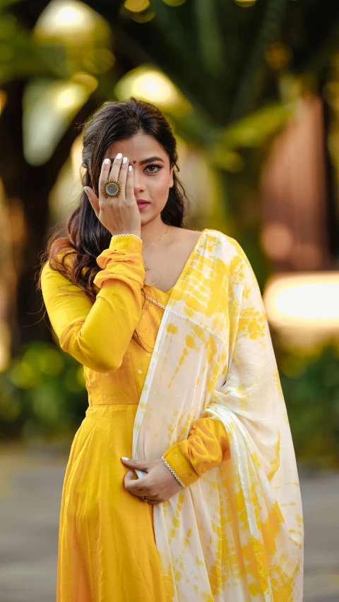 a woman in a yellow and white outfit, holding her hand up to her eye