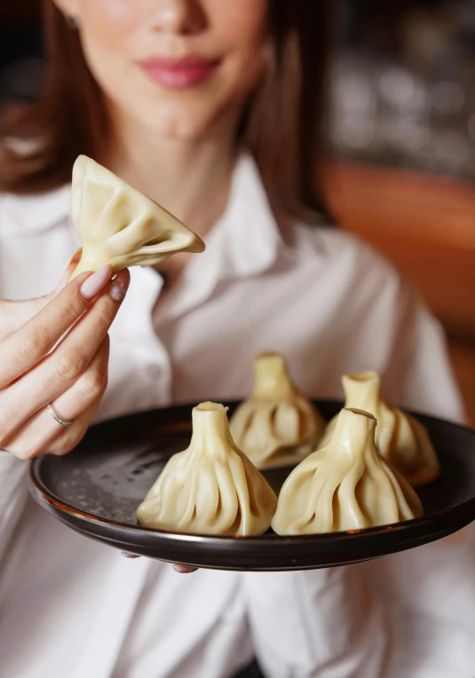 woman holding up plate of small dumplings with sauce