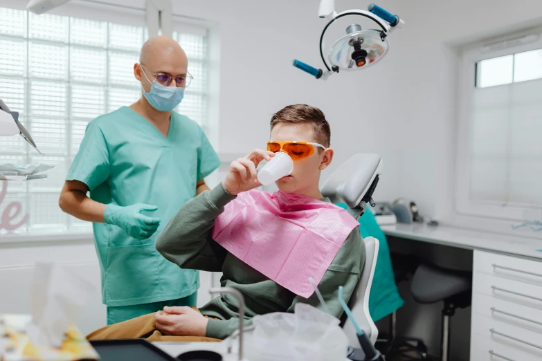 a male dentist examining a young patient who is wearing a face mask