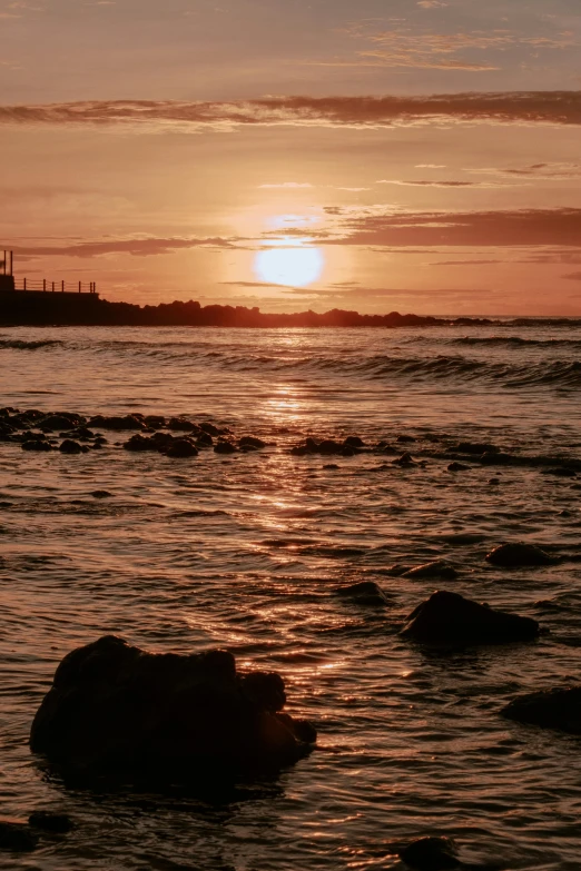 a sunset over the water with a lighthouse in the distance