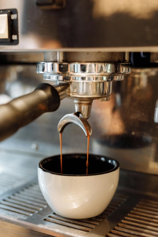 an espresso machine is filling coffee into a white cup